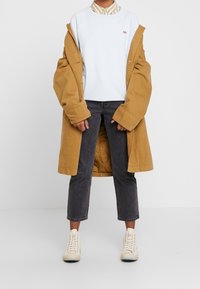 Béžový dlouhý kabát přes světle modrou mikinu, šedé krátké džíny a béžové vysoké tenisky, na mikině je malé logo.