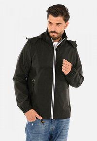 Giacca nera impermeabile con chiusura a zip, polsini elasticizzati e dettagli bianchi. Presenta un cappuccio e due tasche laterali. Traspirante al tatto.