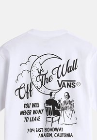 Camiseta blanca de algodón con estampado gráfico negro de esqueletos en una mesa, luna creciente y texto "Off the Wall Vans".