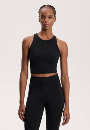 Černý cropped sportovní top s kulatým dekoltem a závodním střihem, zkombinovaný s černými legínami s vysokým pasem a zakřivenými švy.