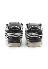 Sneaker a strisce zebra in bianco e nero con finitura texture, dotati di dettagli in pelle nera, borchie metalliche e cuciture viola.