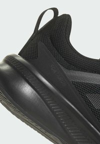 Chaussure de sport noire avec une tige en mesh texturé et une semelle en caoutchouc lisse. Comprend une languette au talon et une semelle extérieure à motif pour une meilleure adhérence.