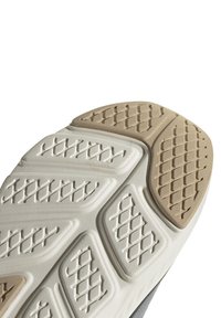 Suela de una zapatilla beige y blanca que muestra una superficie texturizada con patrones en forma de diamante en las áreas del talón y del antepié.