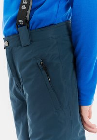 Marineblauwe geïsoleerde broek met een gladde textuur, voorzien van een zak met rits en verstelbare banden bij de taille voor een veilige pasvorm.