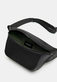 Czarna torebka crossbody z sztucznej skóry z zamkiem błyskawicznym. Wnętrze wyłożone ciemnozielonym materiałem, z widocznym logo marki. Regulowany pasek.