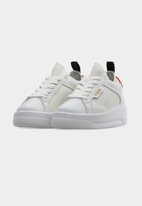 Ζευγάρι λευκά αθλητικά παπούτσια με κορδόνια, διάτρητα πάνελ από δίχτυ, παχιά πέλματα, μαύρες θηλιές στη φτέρνα και μικρή χρυσή ετικέτα στο πλάι, πάνω σε απλή φόντο.