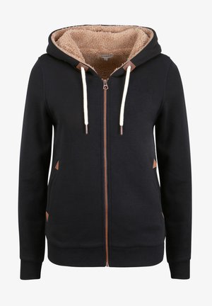 Sudadera con cremallera negra y forro de polar beige, con acentos de cuero marrón, cordones blancos y bolsillos laterales. Textura suave.