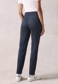 Marineblauwe gestreepte broek met een elastische tailleband en taps toelopende benen, gemaakt van een zachte stof. Gevergd met witte sneakers.