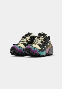 Chaussures de trail running présentant un upper beige, des lacets noirs et une semelle colorée avec des accents violets, turquoise et bleus. Semelle extérieure texturée pour une meilleure adhérence.