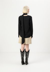 Maglione nero a coste con un lungo dettaglio a sciarpa, gonna beige e stivali cowboy neri con ricami floreali argentati. Sfondo pulito e minimalista.