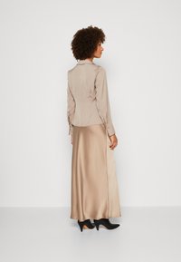 Beige satin paita pitkillä hihoilla ja kauluksella, yhdistettynä samansävyiseen maksihameeseen. Mustat korkeat kengät täydentävät asua.