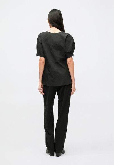 Fekete, puffos ujjú felső lekerekített nyakkivágással, egyenes szárú fekete nadrággal párosítva. Sima anyag, letisztult dizájn, tiszta vonalak.