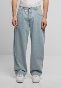 Hellblaue, weit geschnittene Jeans aus Denim, mit einer Vorderseite zum Schließen, Taschen und einem gelben gestickten Logo am Bund.
