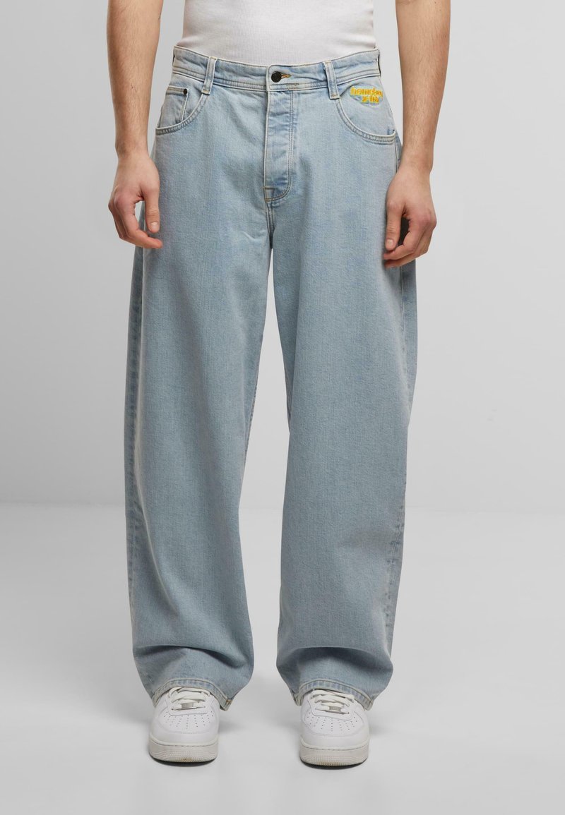 Hellblaue, weit geschnittene Jeans aus Denim, mit einer Vorderseite zum Schließen, Taschen und einem gelben gestickten Logo am Bund.