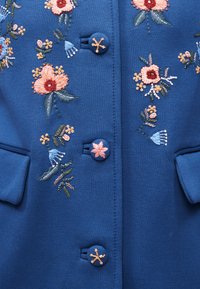 Μπλε ύφασμα με ροζ, πορτοκαλί και πράσινη κεντητή floral διακόσμηση και αντίστοιχα κεντημένα κουμπιά με διάφορα σχέδια λουλουδιών.