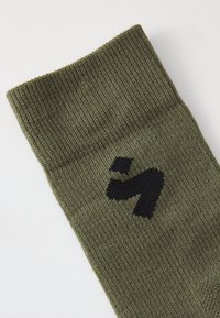 Olivzaļš zābaku elastīgais zeķes audums ar ribota tekstūra, sānos ar melnu logotipu. Mīksts adījuma materiāls stiepjās līdz aprocei.