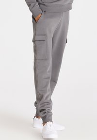 Šedé tepláky vyrobené z měkké tkaniny, s bočními kapsami a zúženými manžetami, doplněné bílými teniskami.