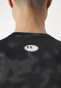 Musthave mustar-säriga spordipait, millel on sile tekstuur ja valge ääristusega ümmargune logo seljal, millel on gradient kujundus.