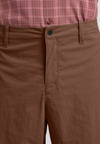 Bruine broek van lichtgewicht stof, met een gestroomlijnd ontwerp, een platte voorkant en een zwarte knop op de taille.