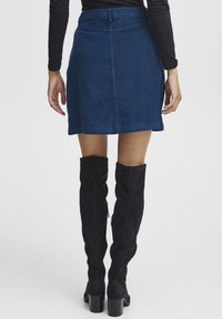 Blauwe corduroy rok met een rechte snit, op mid-dij lengte. Gedragen met zwarte over-de-knie laarzen, met een chunky hak en textielstof.