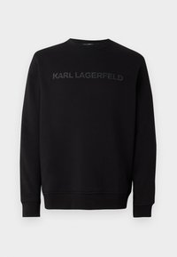Črna majica s kapuco iz mehkega materiala, z okroglim izrezom in dolgimi rokavi. Spredaj je prikazan tonalen logo "KARL LAGERFELD".