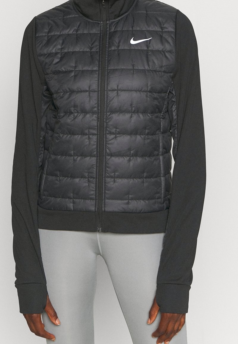 Gilet rembourré noir avec un motif matelassé, fermeture éclair et longues manches noires. Présente un petit logo Nike blanc sur la poitrine.