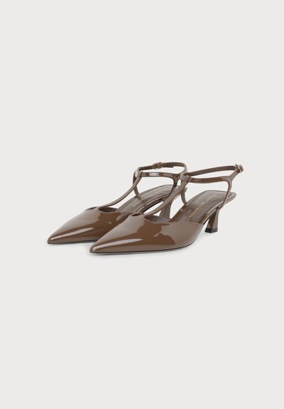 Γυαλιστερά καφέ πέδιλα slingback με μυτερή μύτη, λουράκια στον αστράγαλο και χαμηλό χοντρό τακούνι σε απλό φωτεινό φόντο.