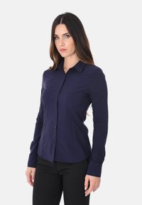 Camicia a maniche lunghe blu navy con bottoni, realizzata in tessuto liscio, con colletto a punta e design aderente, caratterizzata da una chiusura con bottoni completa e cuciture strutturate.