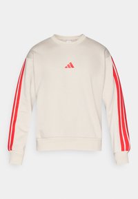 Beige hosszú ujjú pulóver piros háromcsíkos díszítéssel az ujjakon és egy kis piros Adidas logóval a mellkas közepén.