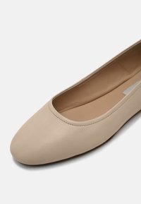 Ballerines en cuir beige avec un bout rond et un design minimaliste. Texture lisse et ouverture élastiquée pour un enfilage facile.
