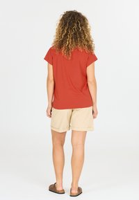 Rød kortærmet skjorte, beige shorts og brune slip-on sko. Skjorten er glat, shortsene er lette med opfoldede kanter. Set fra ryggen.