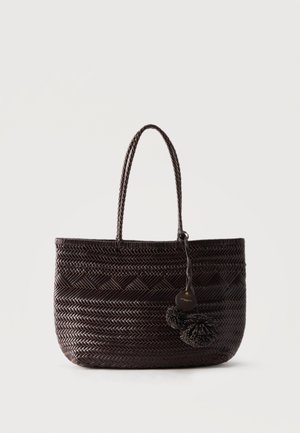 Sötétbarna szőtt bevásárlótáska két fogantyúval, rajta kerek címkével és díszes pomponokkal, egyszerű világos háttér előtt.