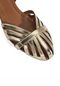 Goldene metallische Slidesandale mit überkreuzten Riemen, offener Zehenpartie und strukturiertem braunem Fußbett. Glatte Oberfläche und flache Sohle.