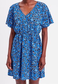 Blauwe bloemenjurk met een V-hals, korte fluttermouwen en een elastische tailleband; het ontwerp bevat kleine paarse en zwarte bloemenpatronen.