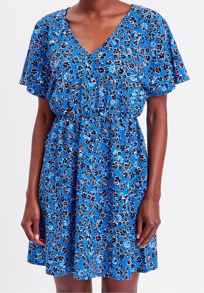 Blauwe bloemenjurk met een V-hals, korte fluttermouwen en een elastische tailleband; het ontwerp bevat kleine paarse en zwarte bloemenpatronen.