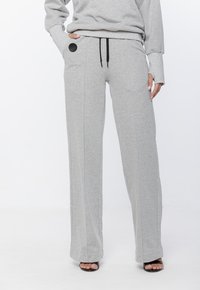 Szare bawełniane długie spodnie dresowe o luźnym kroju, z elastycznym pasem na sznurek, przednimi kieszeniami oraz okrągłym czarnym haftem po boku.