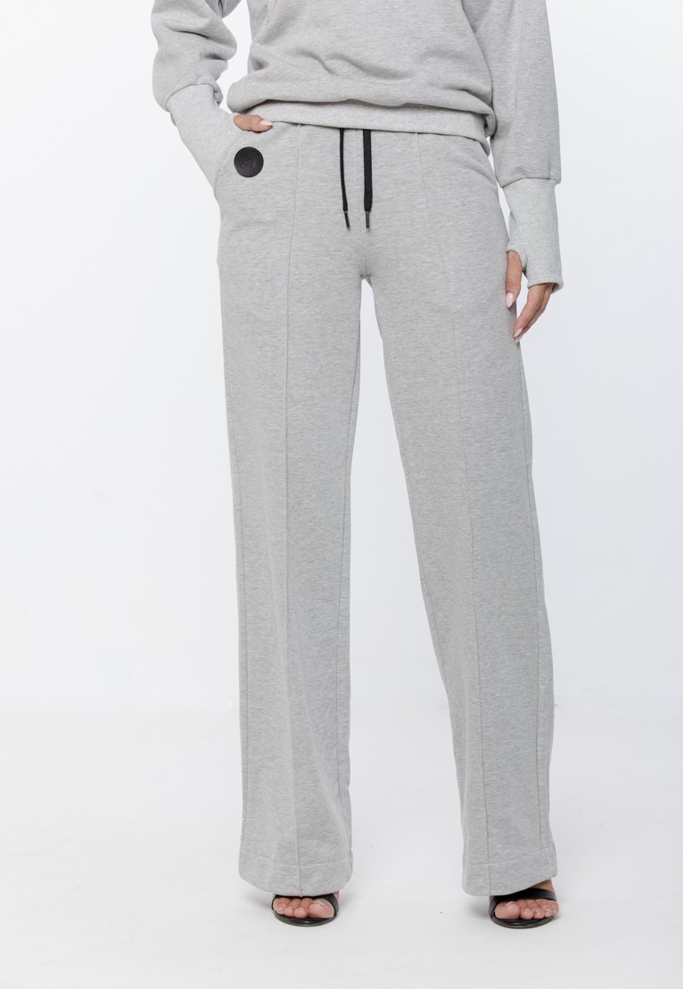 Szare bawełniane długie spodnie dresowe o luźnym kroju, z elastycznym pasem na sznurek, przednimi kieszeniami oraz okrągłym czarnym haftem po boku.