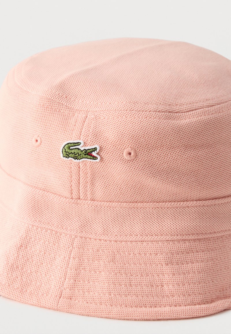 Hellrosa strukturierter Bucket-Hut mit kleinem grünem Krokodil-Logo vorne bestickt.