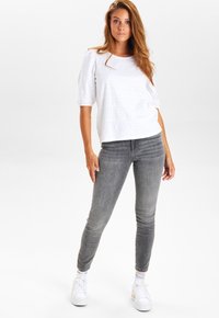 White short-sleeve top with textured details, paired with gray skinny jeans and white sneakers with multicolored striped socks.