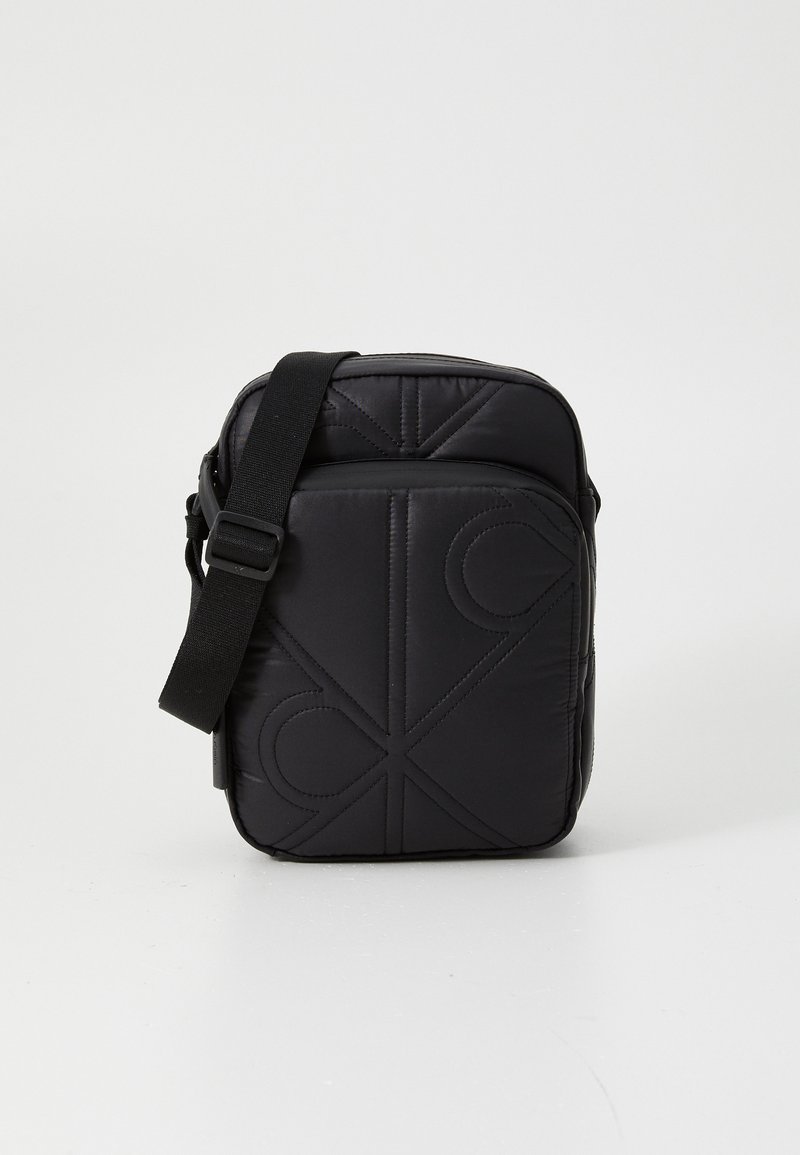 Black quilted crossbody bag featuring a geometric design, adjustable strap, and zipper closure. Made from durable, textured fabric.