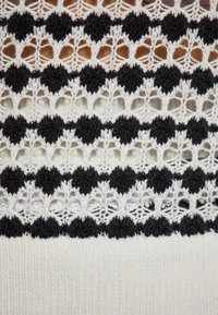Strickkleid mit abwechselnden schwarzen und weißen Häkelmustern in Herzform. Weiche Textur, detailliertes Durchbruchsdesign.