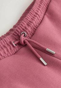 Primo piano della fascia elastica rosa con coulisse e terminali metallici su pantaloni o pantaloncini in tessuto casual.