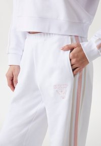 Witte katoenen trainingspak in een blend, bestaande uit een cropped top en een broek met roze en beige strepen, geborduurd logo en zijzakken.