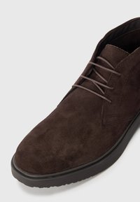 Dark brown suede ankle boot with a rounded toe, lace-up design, and textured surface. Rubber sole with a slight tread pattern.
