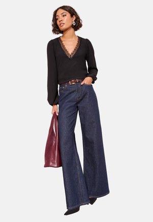 Black long-sleeve top with lace neckline detail, paired with wide-leg dark denim jeans and a burgundy handbag. Textured fabric, relaxed fit.
