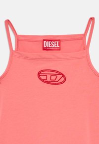 Korallinpunainen toppi ohuilla spagettimehustimilla, jossa on punaisella kirjailtu logo. Pehmeä kangas, klassinen muotoilu vähäisillä yksityiskohdilla.