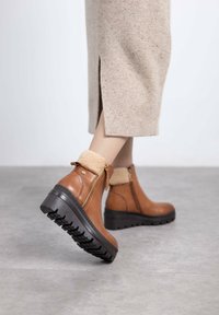 Las botas de tobillo de cuero marrón cuentan con un suave puño color marrón claro, cremallera lateral y una suela gruesa negra con tapas para mayor tracción.