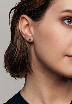 Skrót zielonych kolczyków w srebrze o kwadratowym wykończeniu. Zbliżenie ukazuje klarowność i odbicia kamienia na neutralnym tle.