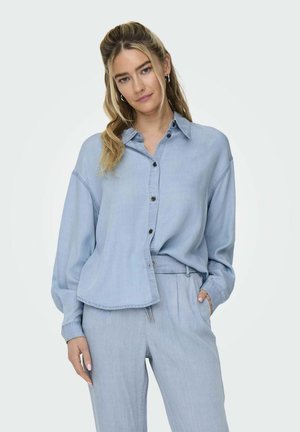 Light blue denim shirt with a relaxed fit, button-down front, and long sleeves. Features a curved hem and visible stitching details.