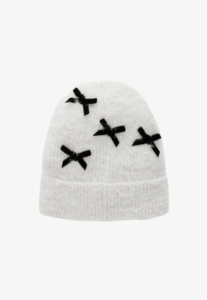 Kootud valge beanie pehme tekstuuriga, mille pinnal on viis musta kangast paela. Disain on ümmargune ja tihedalt istuv.